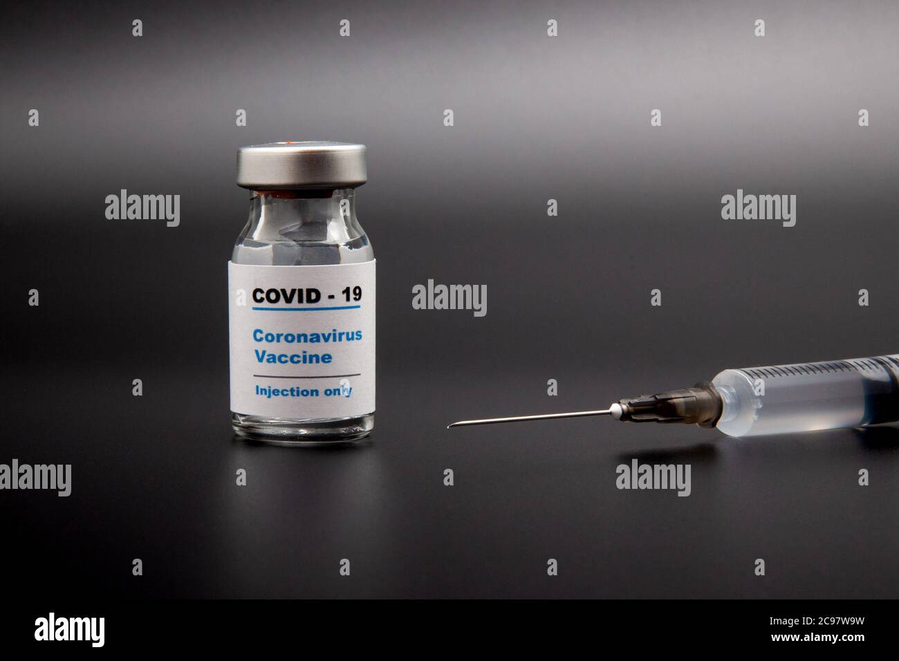 Small vaccine bottle (phial) with a label that read 'Covid - 19 Corona virus Vaccine injection only' & a medical syringe isolated on black Vaccination Stock Photo
