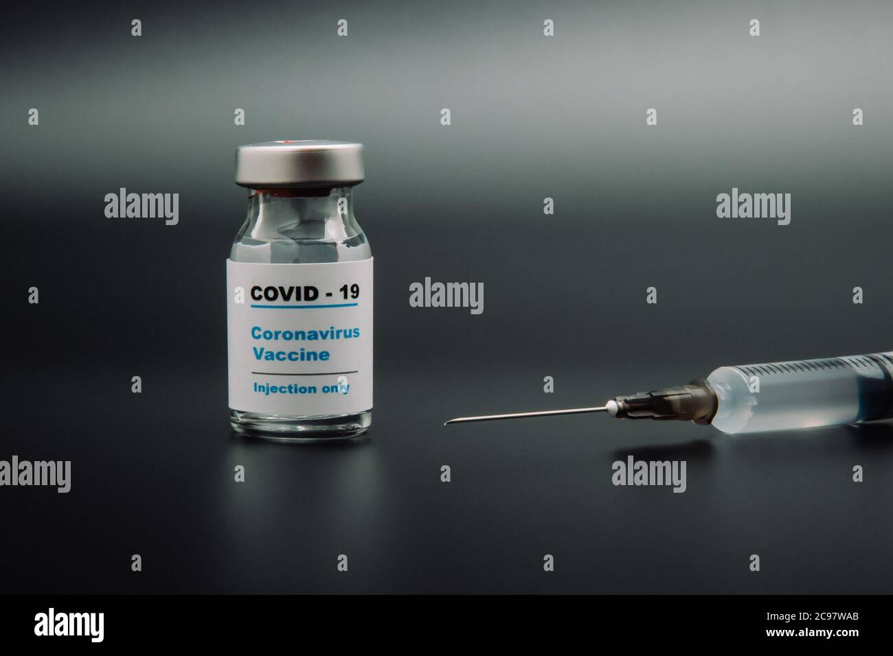 Small vaccine bottle (phial) with a label that read 'Covid - 19 Corona virus Vaccine injection only' & a medical syringe isolated on blue Vaccination Stock Photo