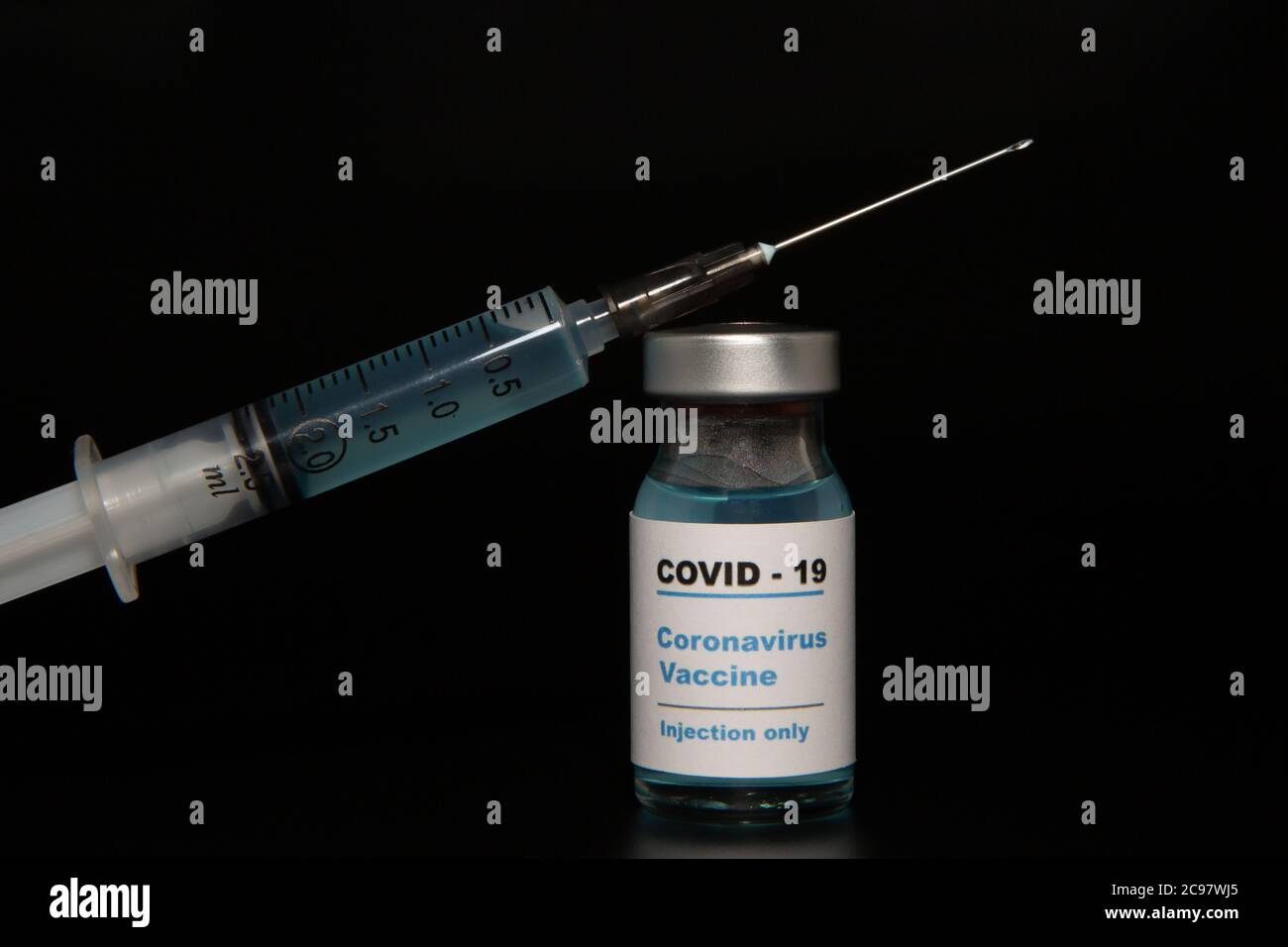 Small vaccine bottle (phial) with a label that read 'Covid - 19 Corona virus Vaccine injection only' & a medical syringe isolated on black Vaccination Stock Photo