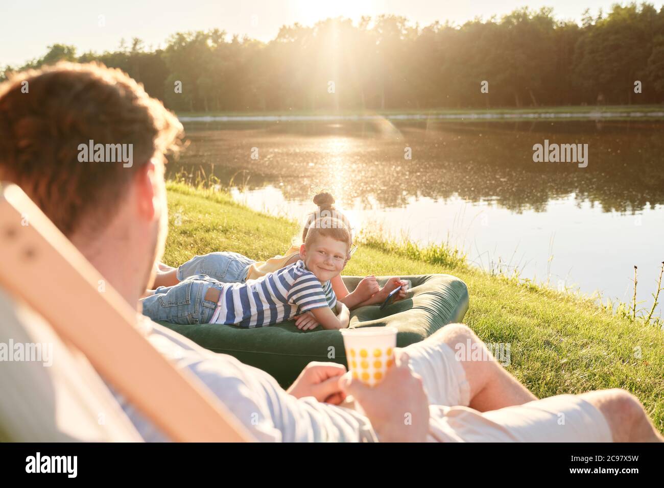 Father and children relaxing by the lake during sunset Stock Photo