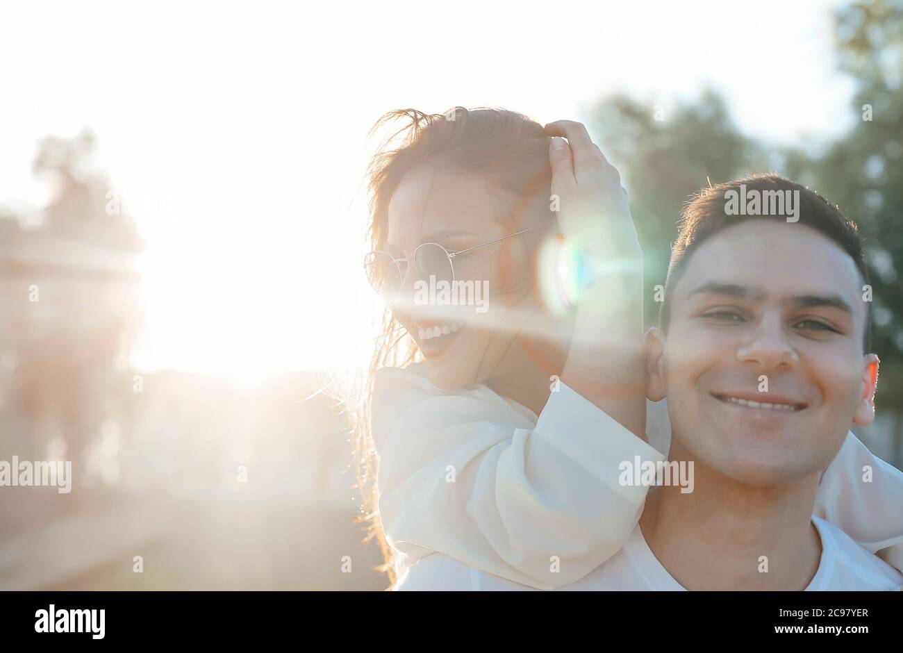 Smiling boyfriend piggybacking delighted girlfriend while enjoying weekend together in summer during sundown Stock Photo
