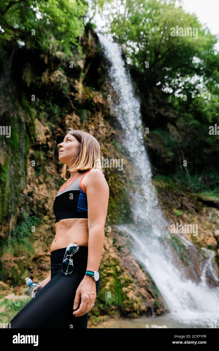 Young female nature explorer standing by the waterfall Stock Photo