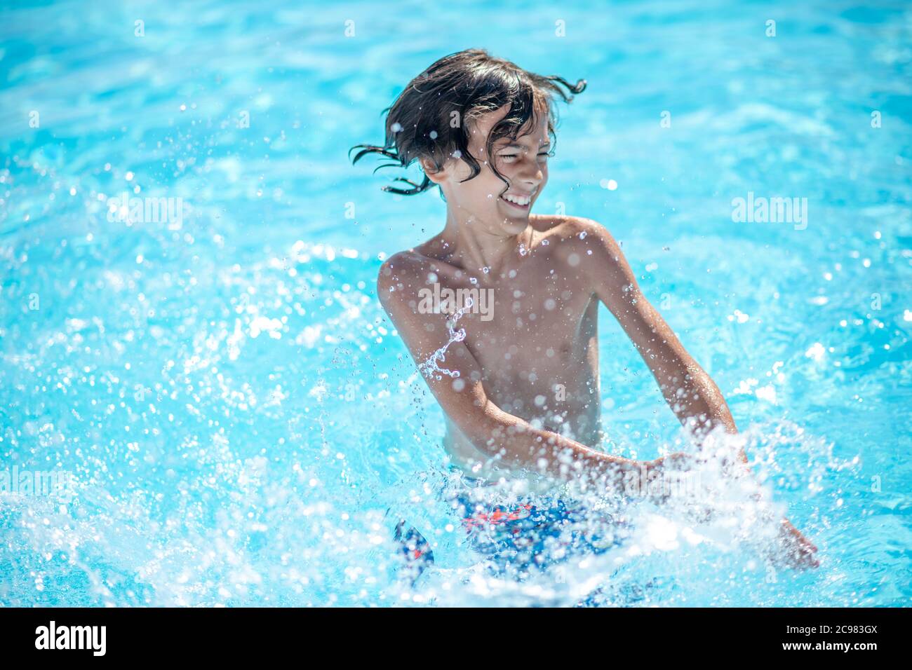 Energetic boy standing in water making splashes Stock Photo