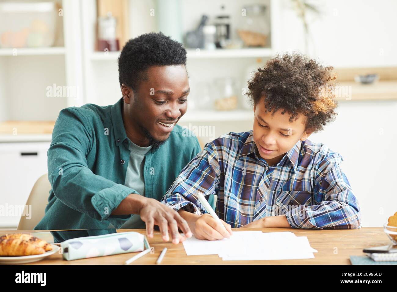 African smiling father helping to his son doing his homework they sitting at the table in the room Stock Photo