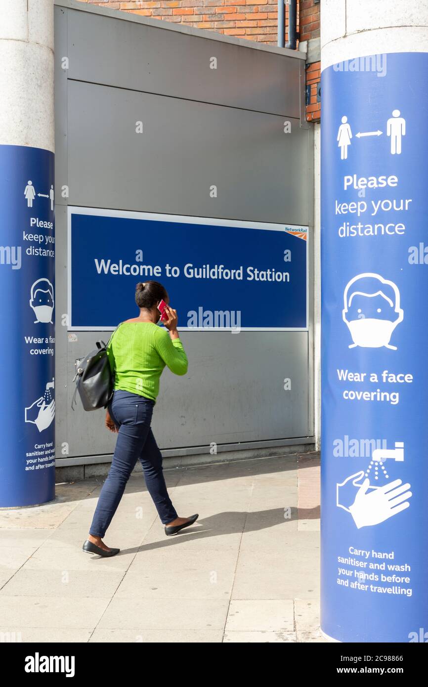 A woman entering Guildford train station between COVID-19 signage, Surrey, England, 29 July 2020 Stock Photo