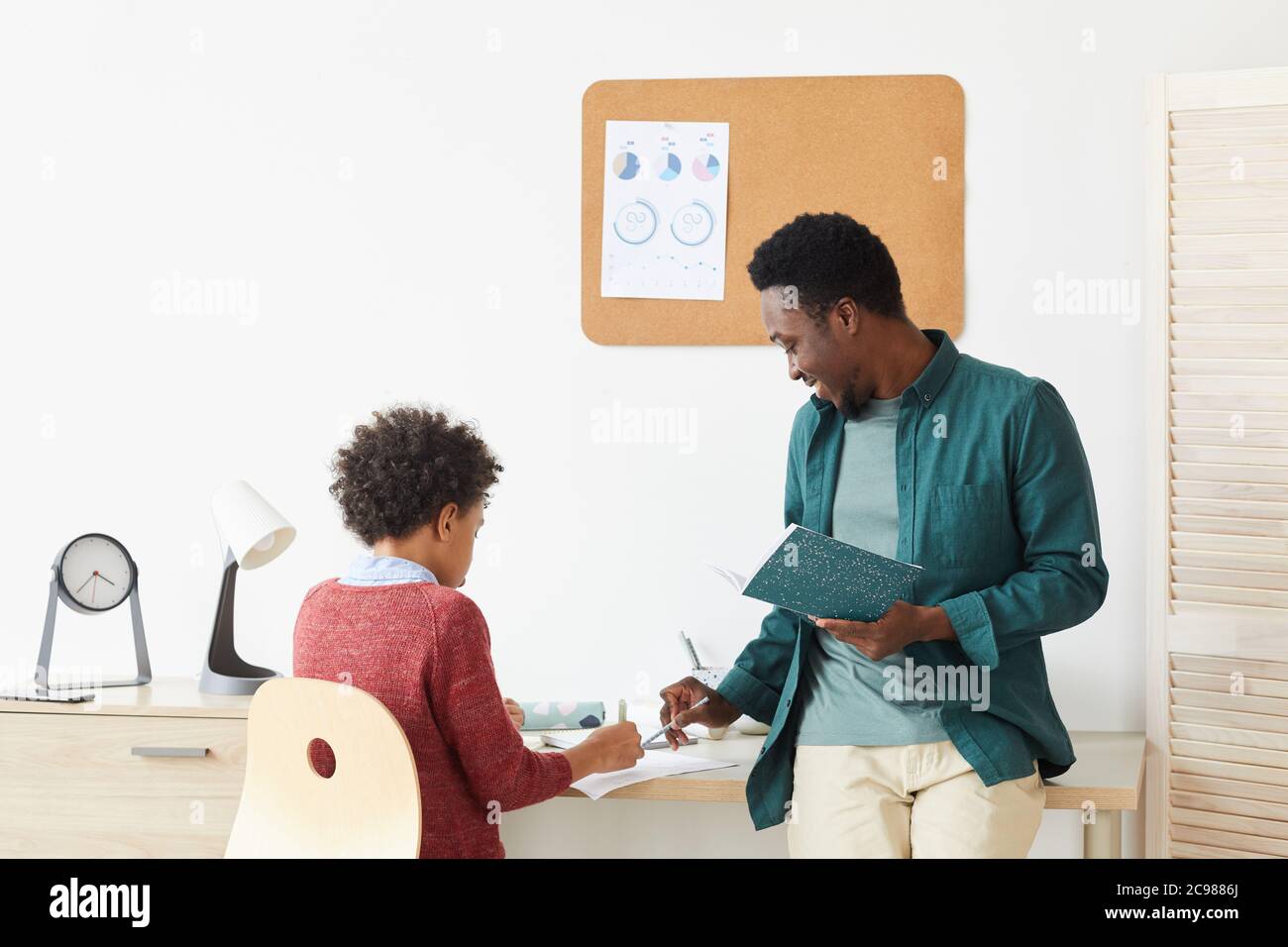 African boy sitting at desk and studying with his teacher at home teacher explaining the new material Stock Photo