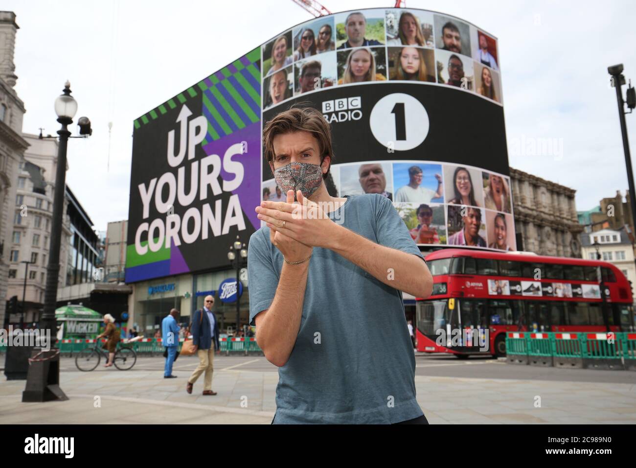 NOTE HAND GESTURE BBC Radio 1 DJ Greg James at Piccadilly Circus, London, as the Radio 1 'Up Yours Corona' campaign is displayed on the Piccadilly Lights screen. The 10 minute long display features one person from every country in the world. Stock Photo