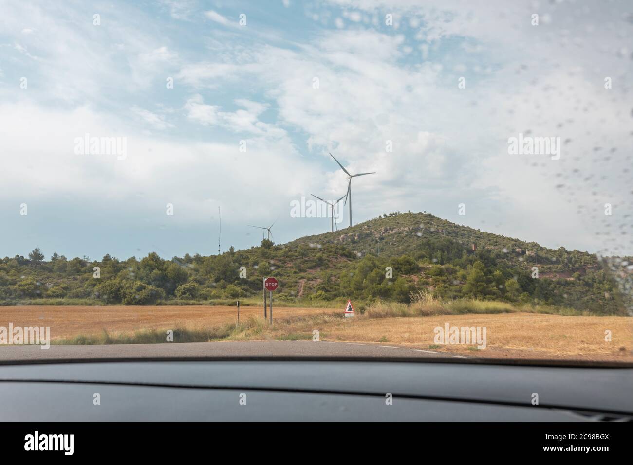 Wind turbines under a cloudy sky seen through the wet glass window of ...