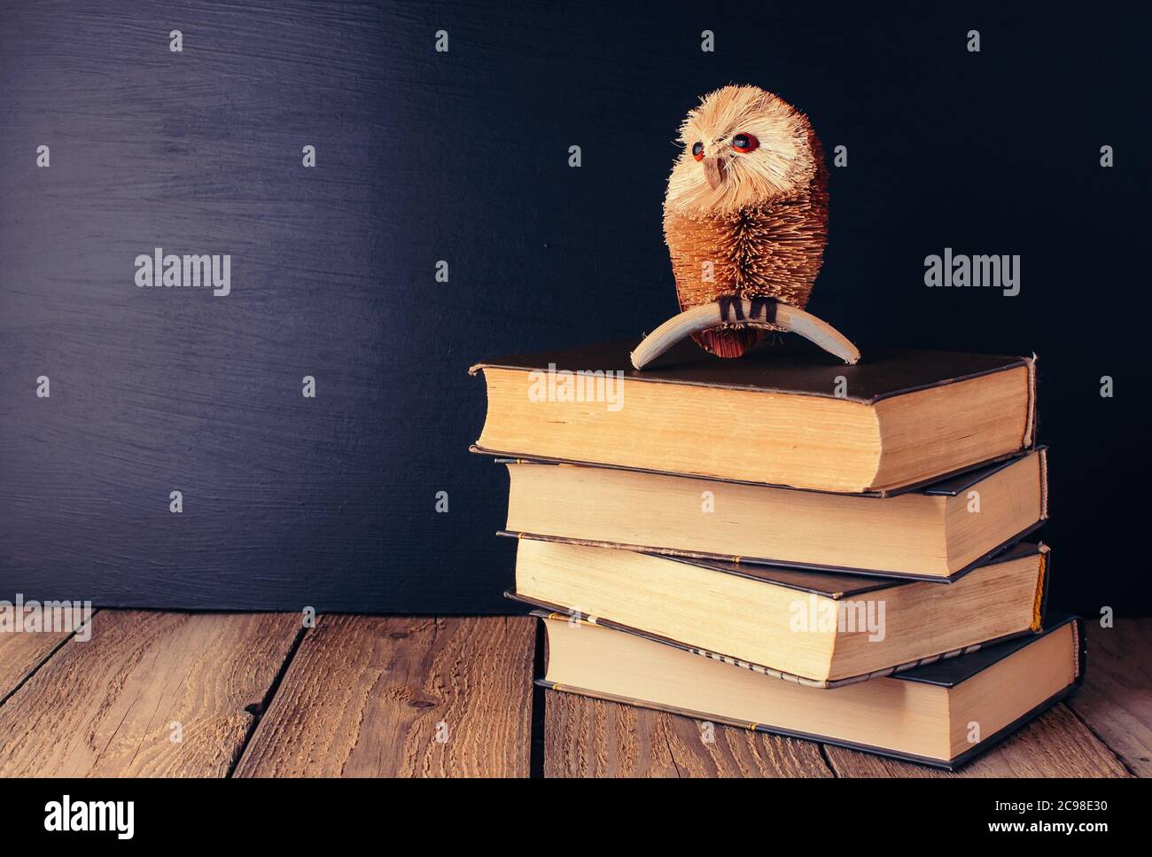 books stacked on a wooden table in a rustic style on the background a school blackboard. Owl on books as a source of wisdom and knowledge. Concept Stock Photo