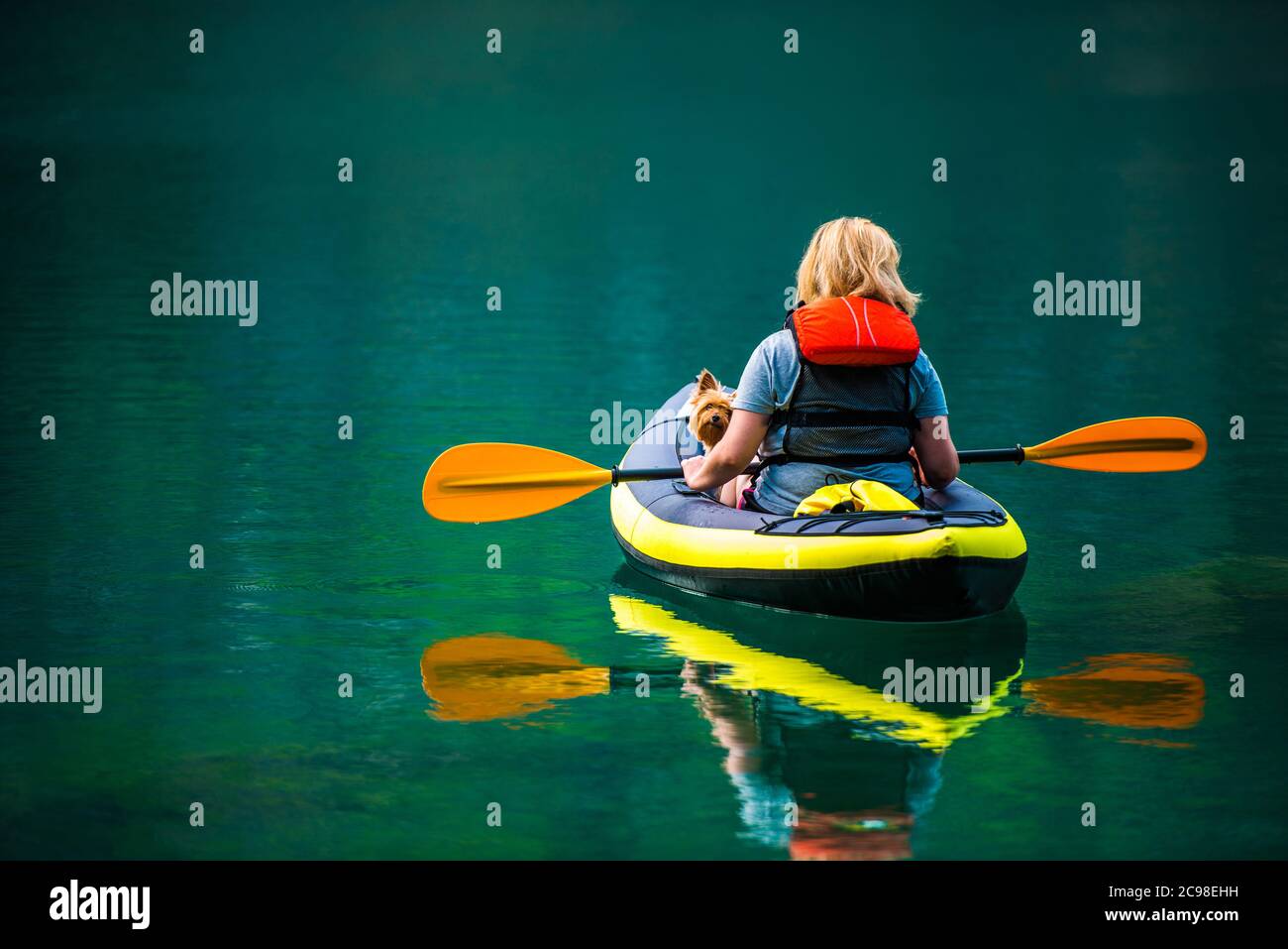 Caucasian Woman Kayaking with Her Australian Silky Terrier Dog During Summer Afternoon. Scenic Turquoise Lake. Stock Photo