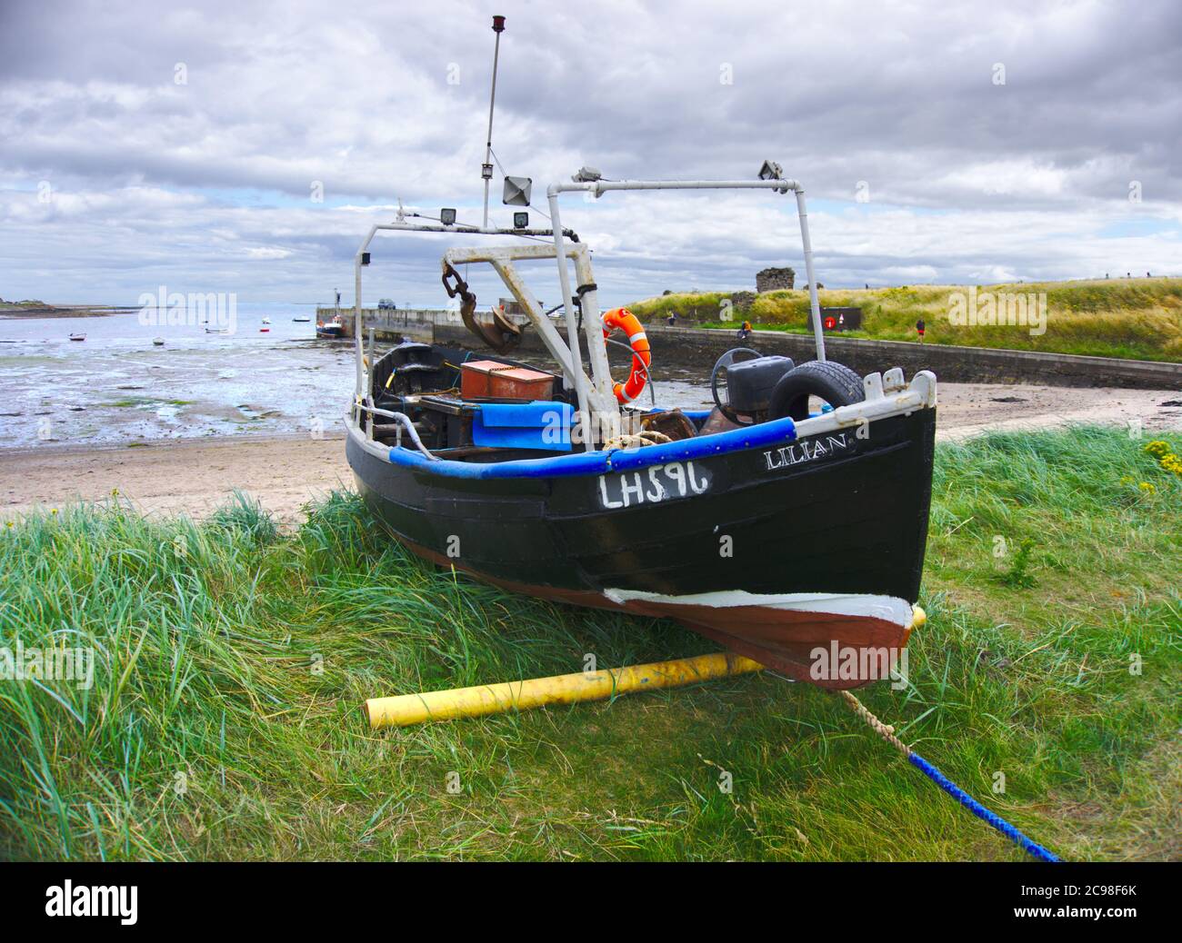 Boat moored on grass at Lindisfarne, with Holy Island harbour in the background. Stock Photo