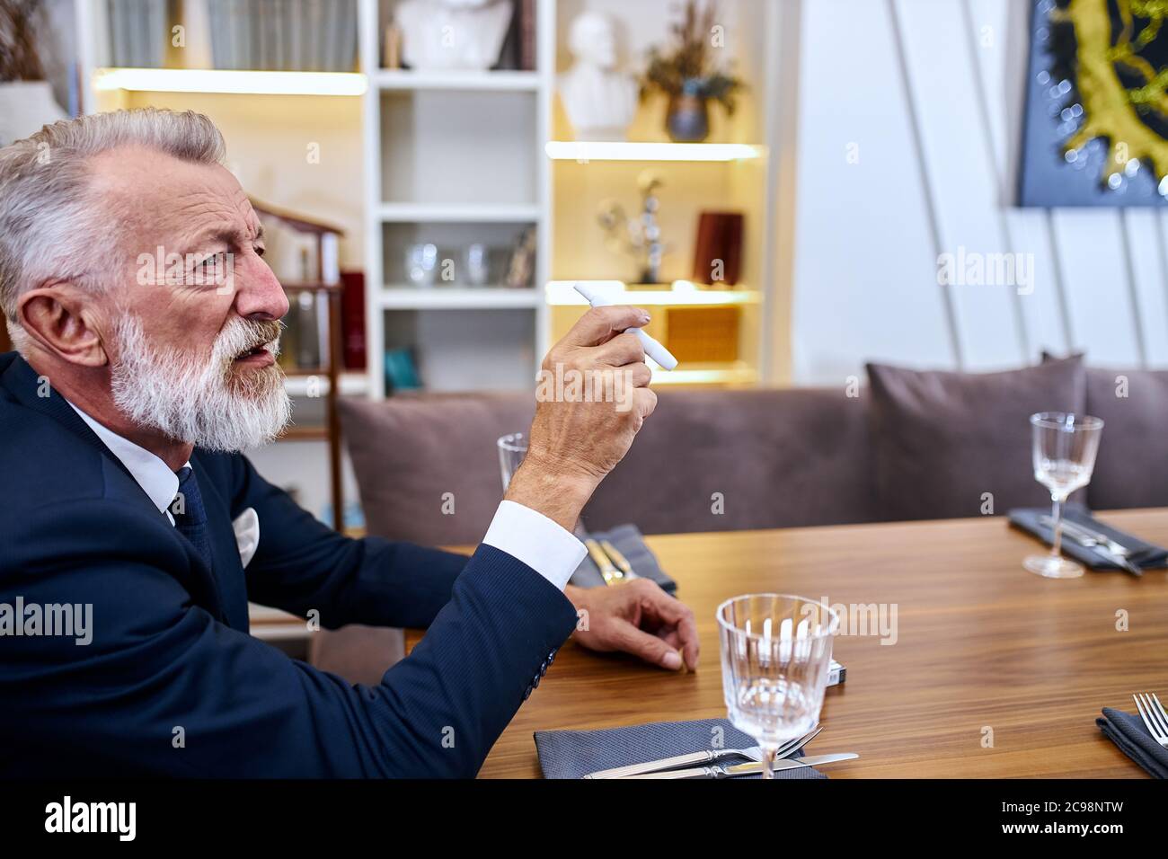 Senior grey haired smoker man keep in hands smoke free-cigarette, explore cigarette, male sits in restaurant Stock Photo