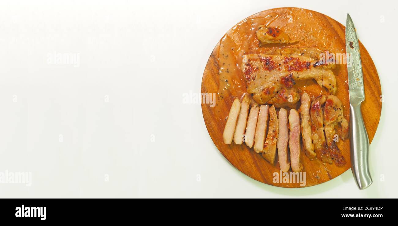 Pork steak with a stainless steel knife placed on the cutting board - white background. Stock Photo
