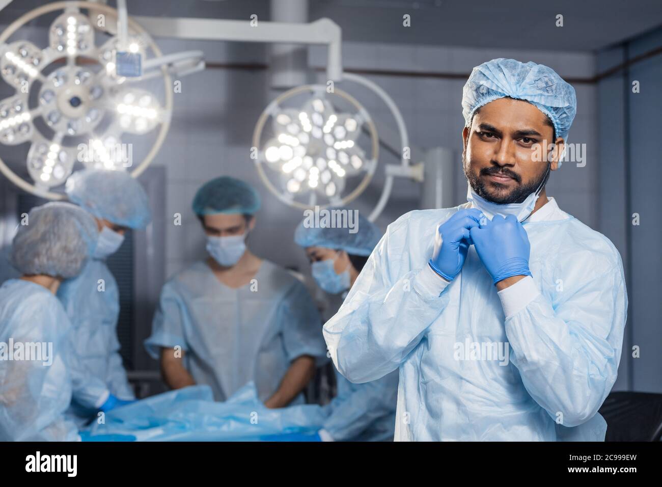 Confident Indian surgeon looking at camera in surgical room hospital, medical doctor wear green