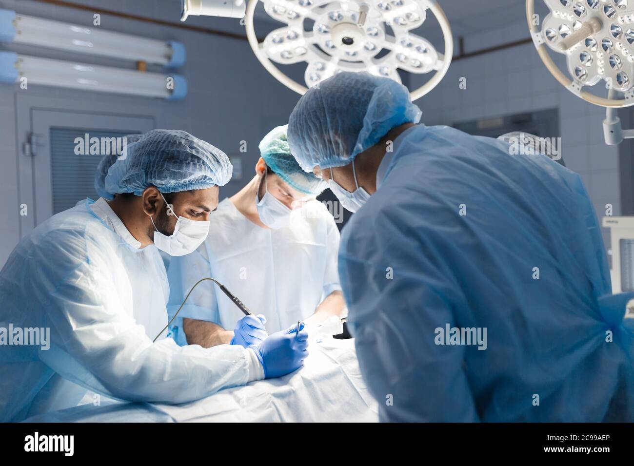 Surgeon doctor operating using electric scalpel wearing blue surgical mask and surgical cap in