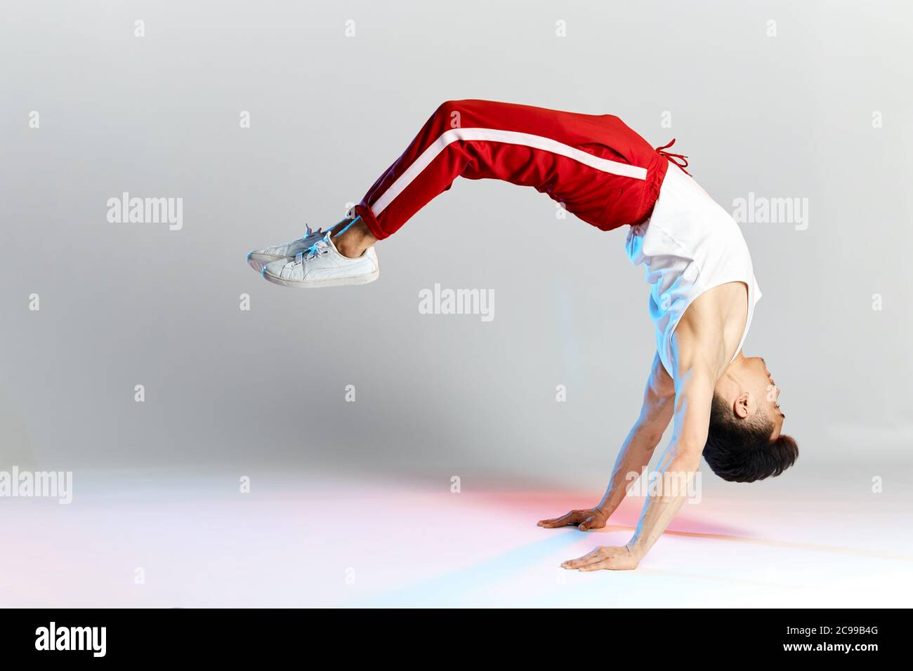 Free style dancer in red sports trousers doing some acrobatic stunts dancing break dance isolated over white studio background Stock Photo