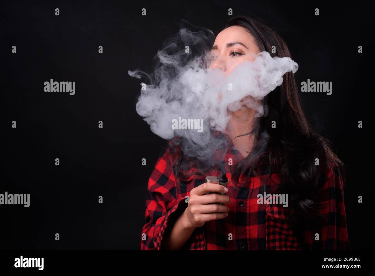 Young beautiful Asian woman vaping against black background Stock Photo