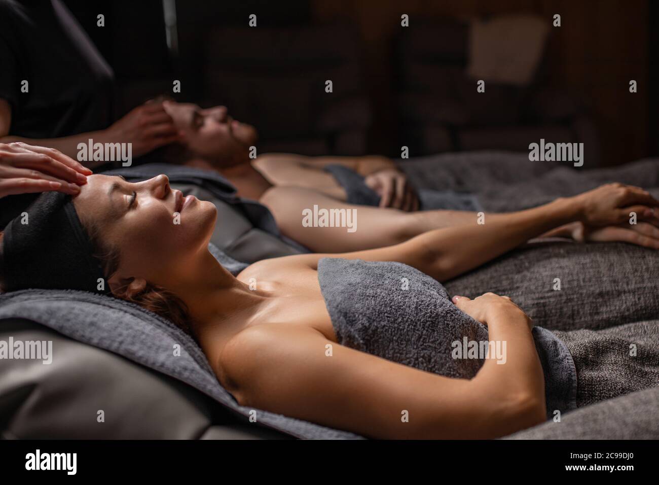 happy married couple lying on massage desks in spa salon, man and woman get cosmetic beauty procedure, take care of skin on head and face, face ligt a Stock Photo