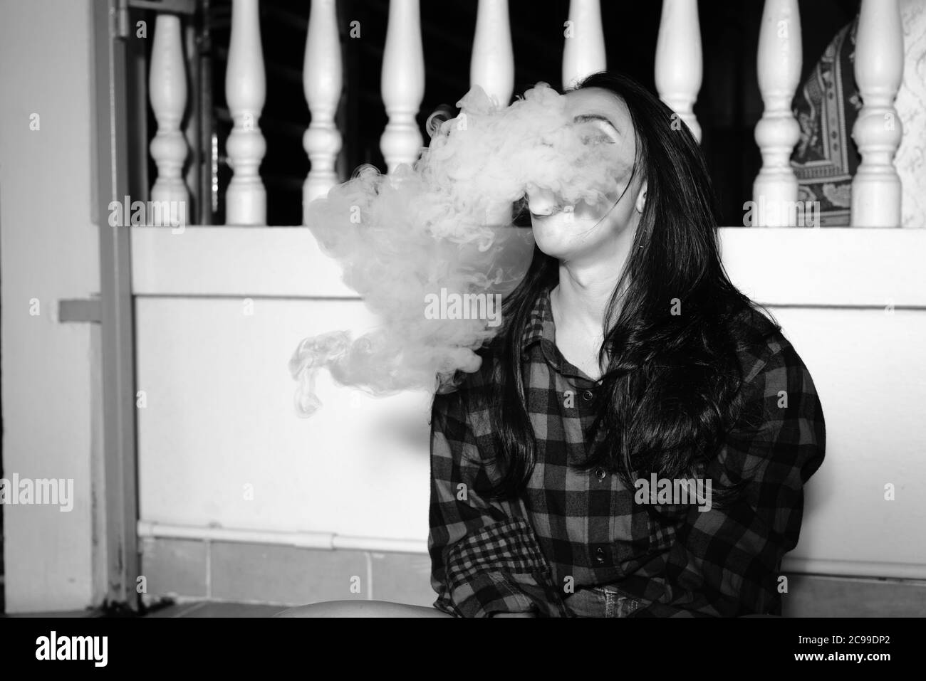 Young beautiful Asian woman vaping at home outdoors in black and white Stock Photo