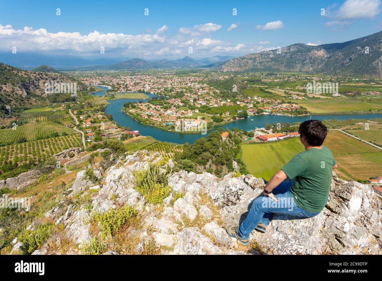 A tourist sits on the summit of Kaunos Akropolü and looks towards the town and river at Dalyan, Turkey Stock Photo