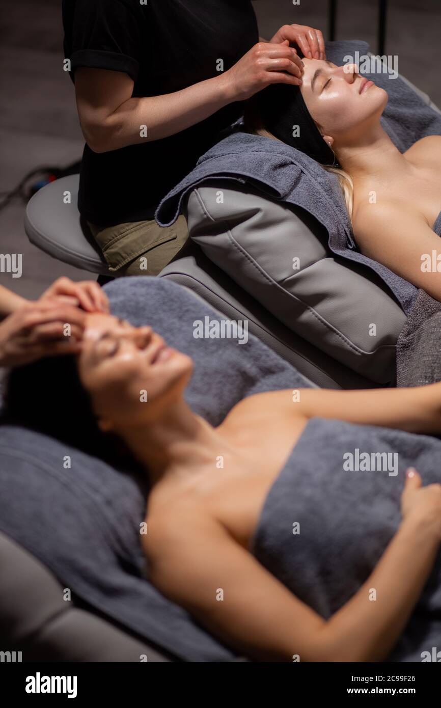 side view on young caucasian woman receiving massage on head in spa salon, attractive women lie with closed eyes, enjoy Stock Photo