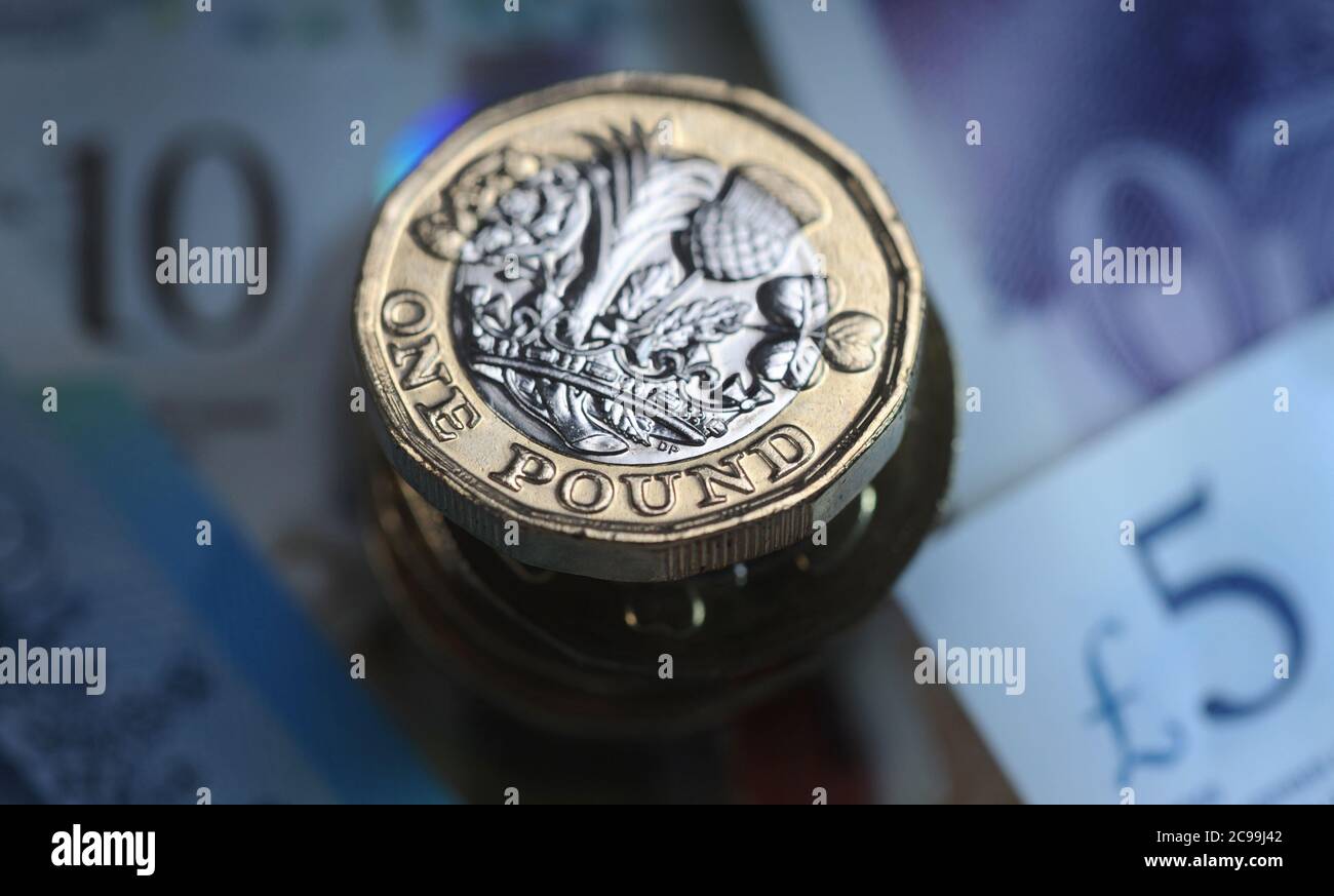 BRITISH ONE POUND COIN WITH MONEY RE THE ECONOMY RECESSION INCOME JOBS WAGES CORONAVIRUS ETC UK Stock Photo