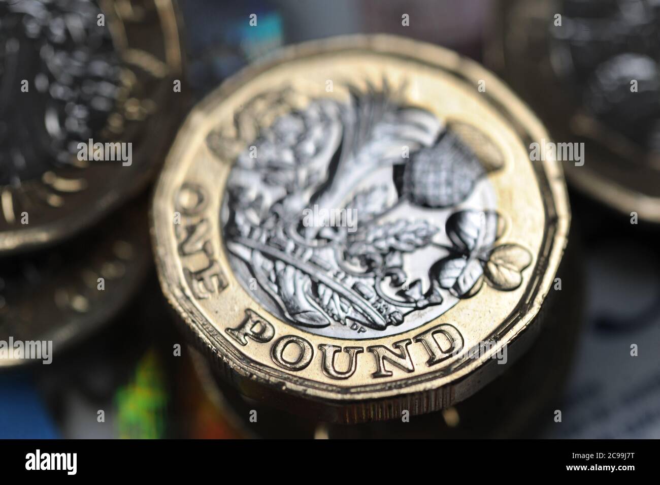 BRITISH ONE POUND COIN WITH MONEY RE THE ECONOMY RECESSION INCOME JOBS WAGES CORONAVIRUS ETC UK Stock Photo