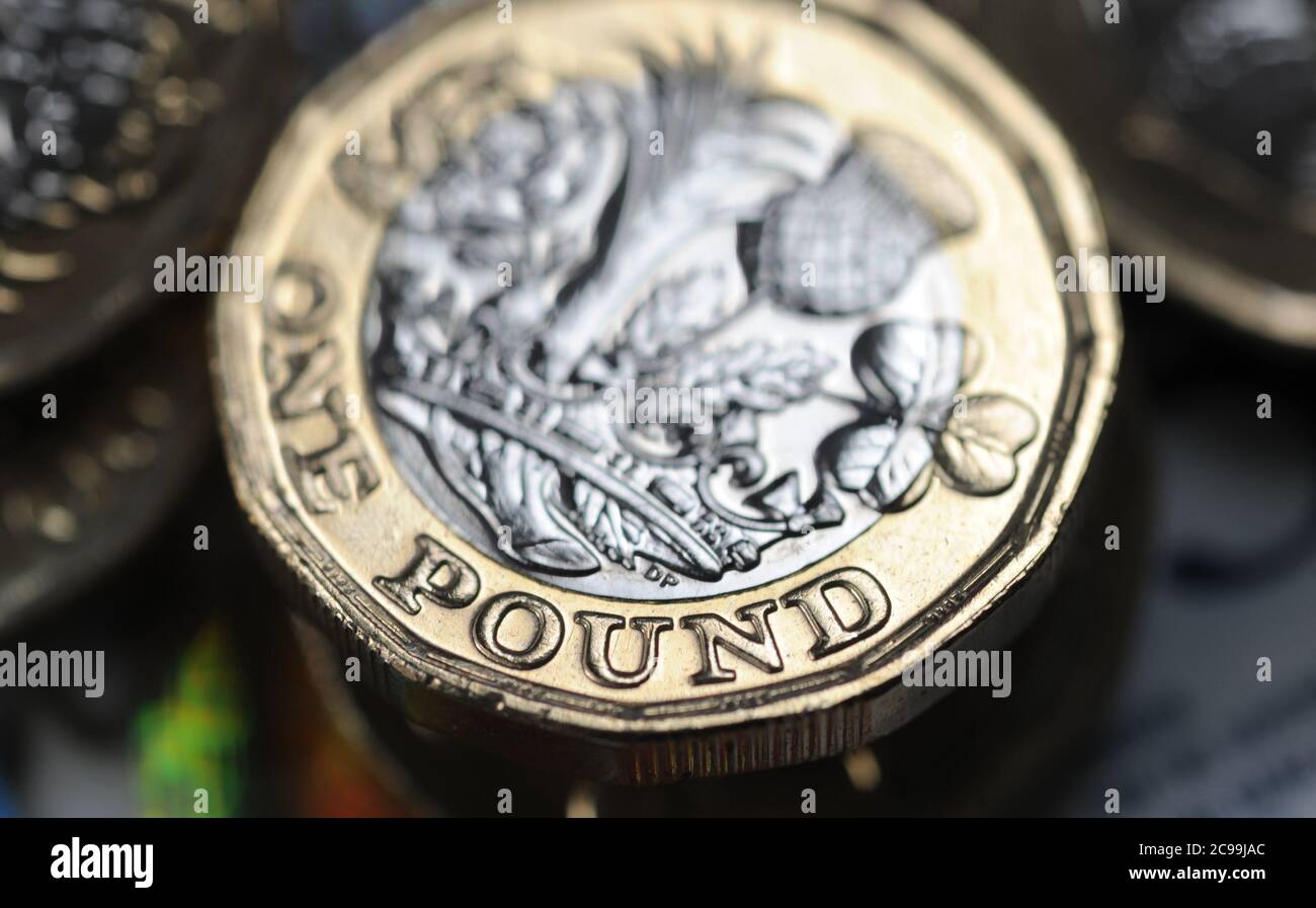 BRITISH ONE POUND COIN WITH MONEY RE THE ECONOMY RECESSION INCOME JOBS WAGES CORONAVIRUS ETC UK Stock Photo