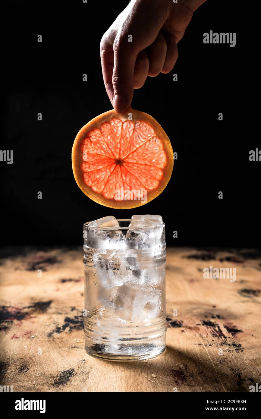 Gin and tonic cocktail recipe, hand holding a grapefruit slice over a