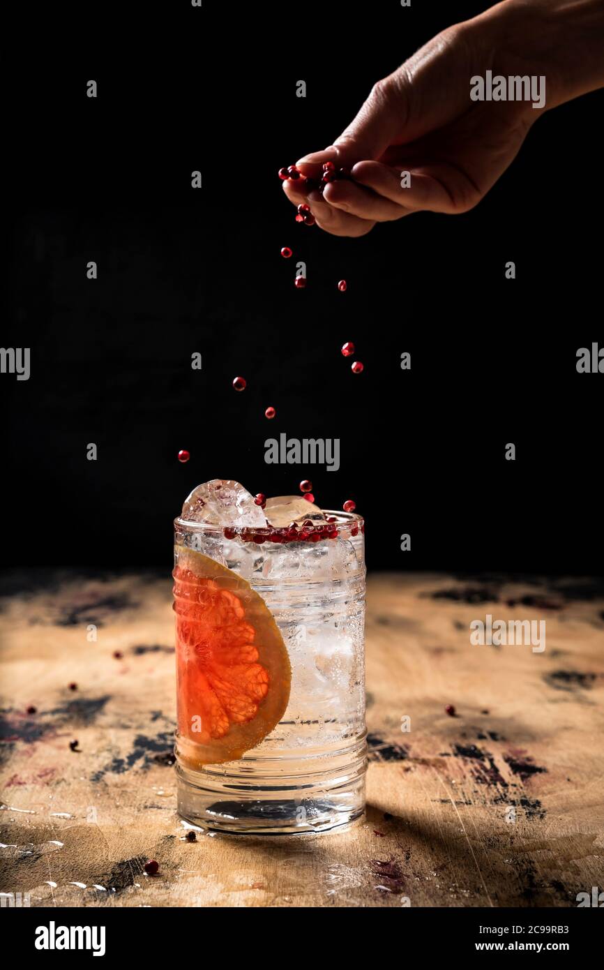 Gin and tonic cocktail recipe, sprinkling a drink with pink peppercorn, highball glass, wooden