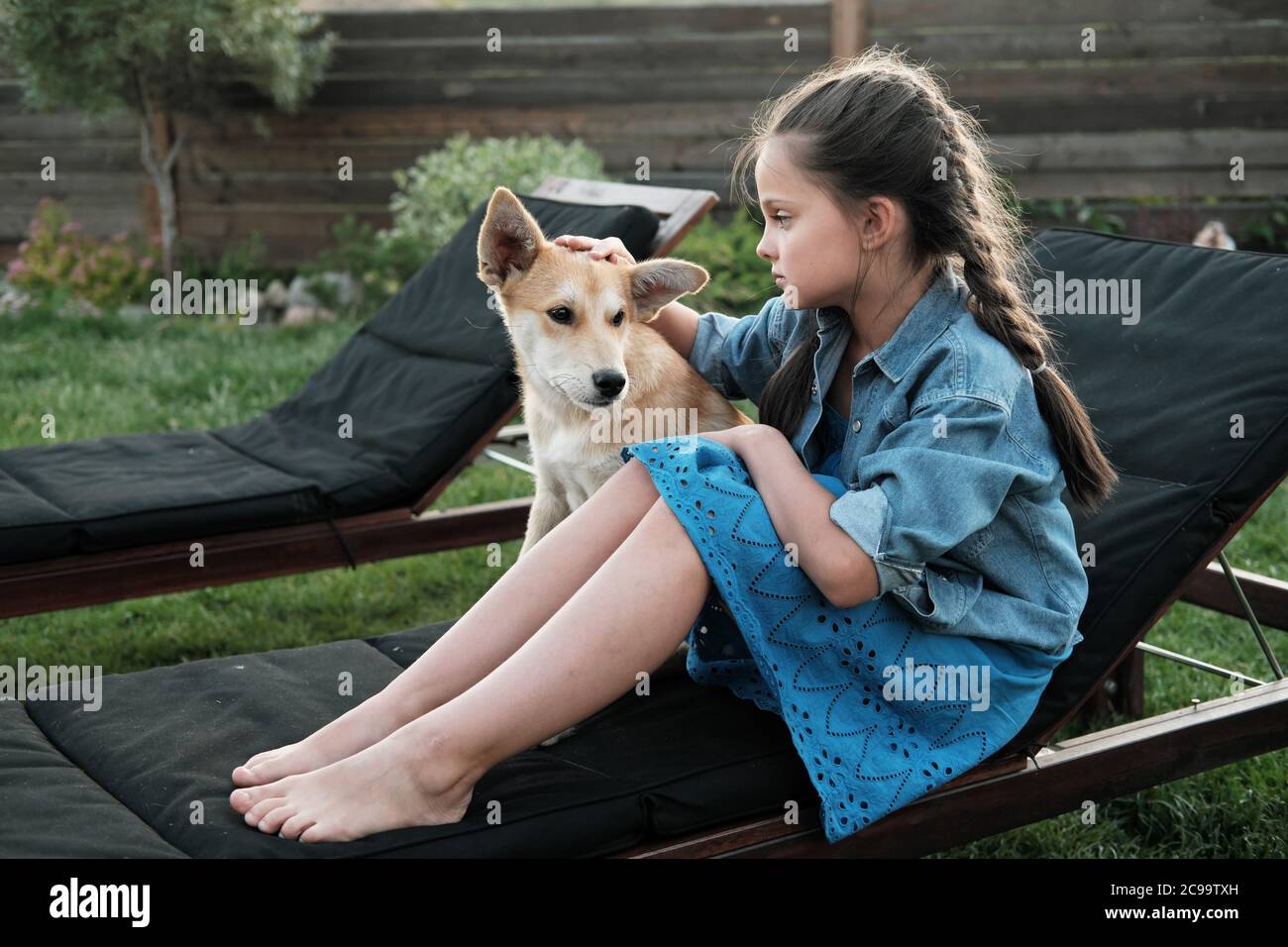 Little girl resting on lounger with her dog outdoors in the country Stock Photo