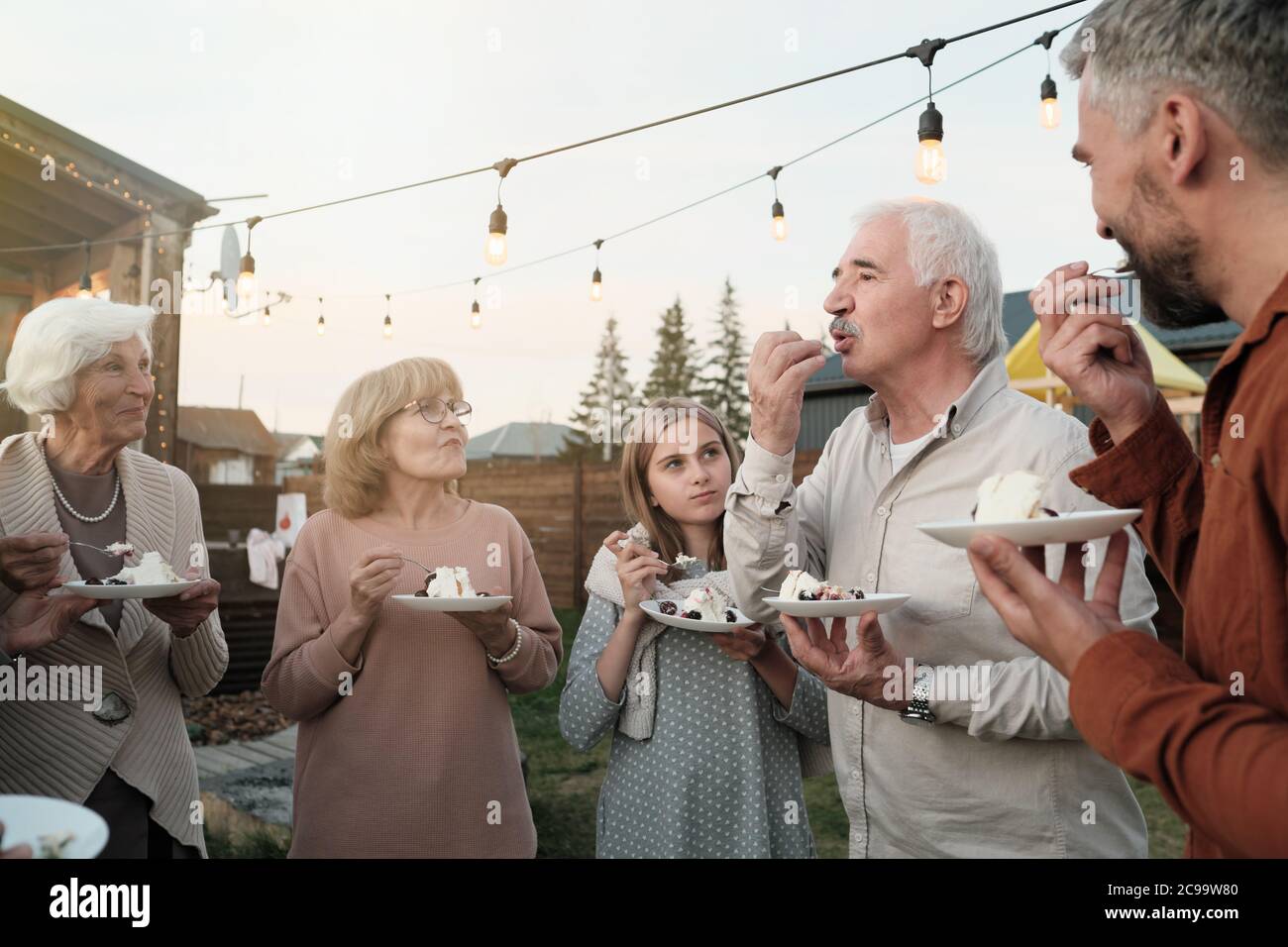 Big family standing in the circle and eating cake together during party on fresh air Stock Photo