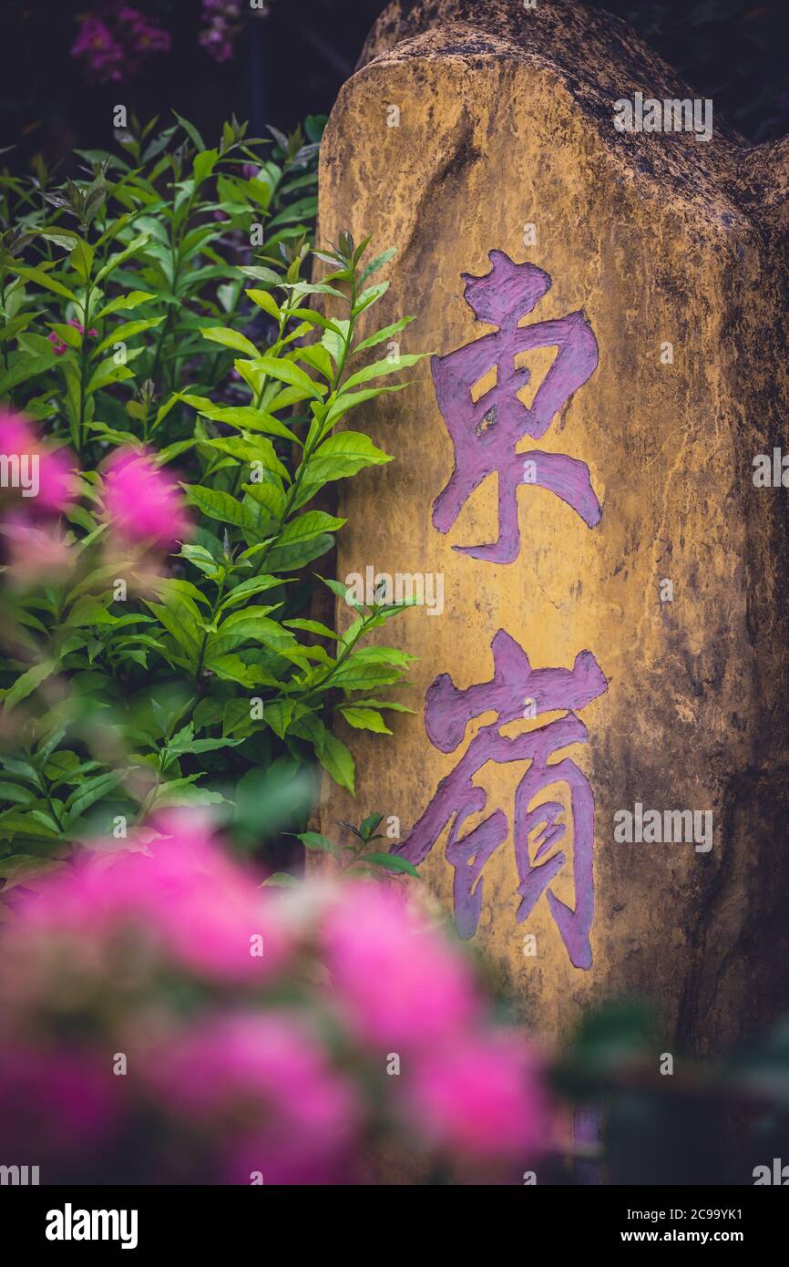 Yangshuo, China - August 2019 : Stone with chinese characters painted in purple colour in the garden Stock Photo