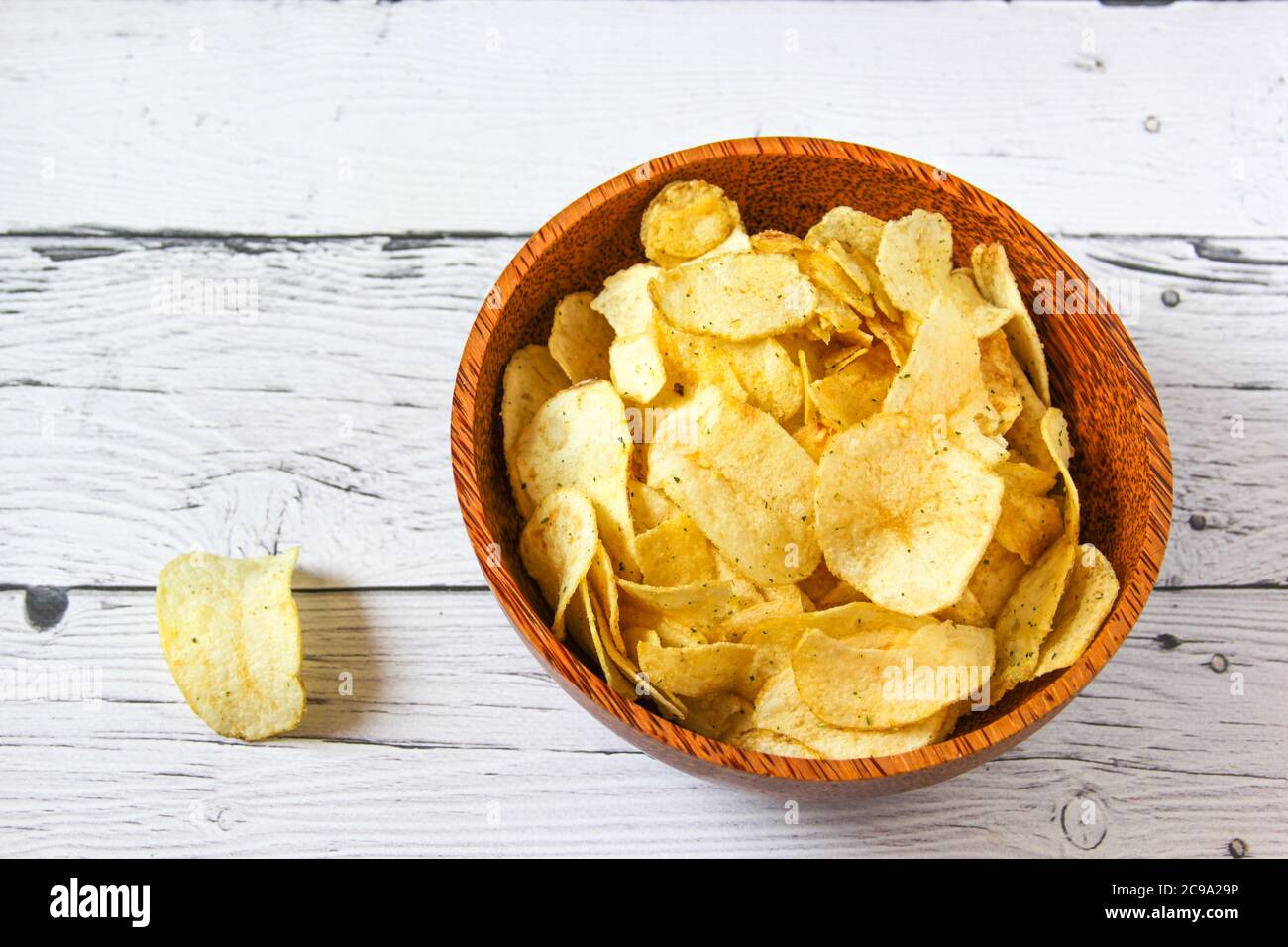Potato chips or crisps in wooden bowl against white wooden background