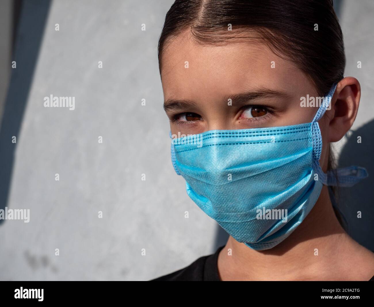 Female teenage girl wearing a blue protective medical face mask. Hazel eyes and brown hair. Antiviral protection during corona virus pandemia concept. Stock Photo