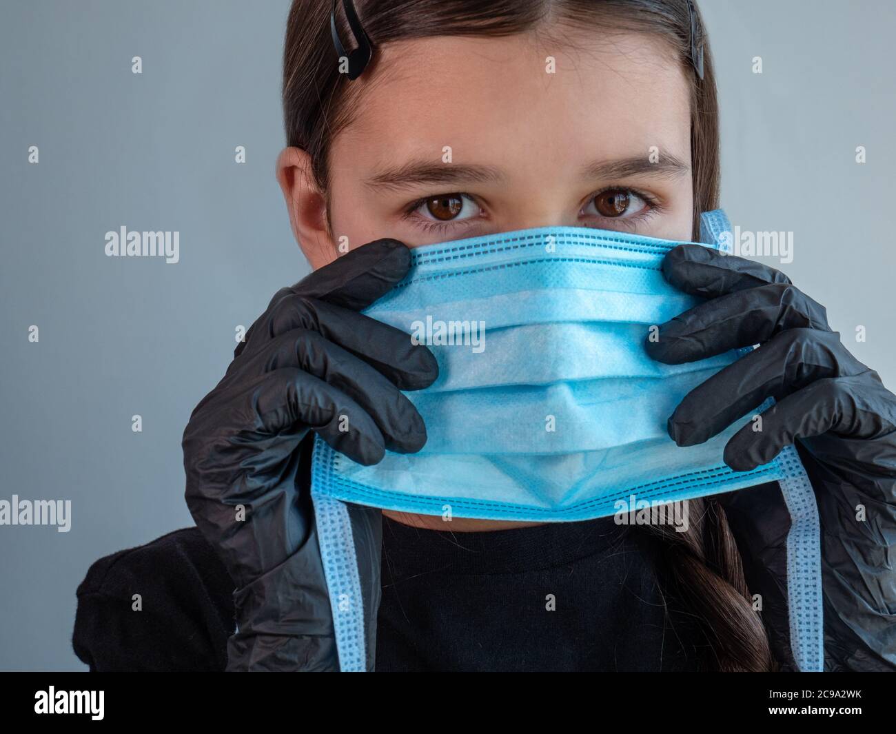 Female teenage girl in black latex gloves holding and fitting on a blue protective medical face mask. Eyes closed. Antiviral protection during covid. Stock Photo