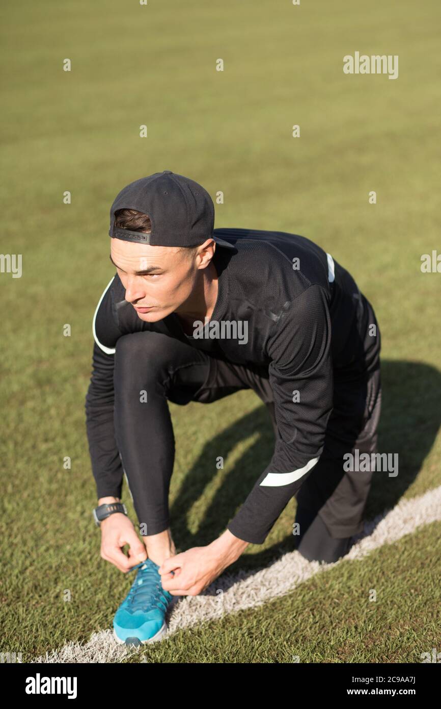slim fit guy sitting on the grass and lacing up shoes while work out. full length side view shot Stock Photo