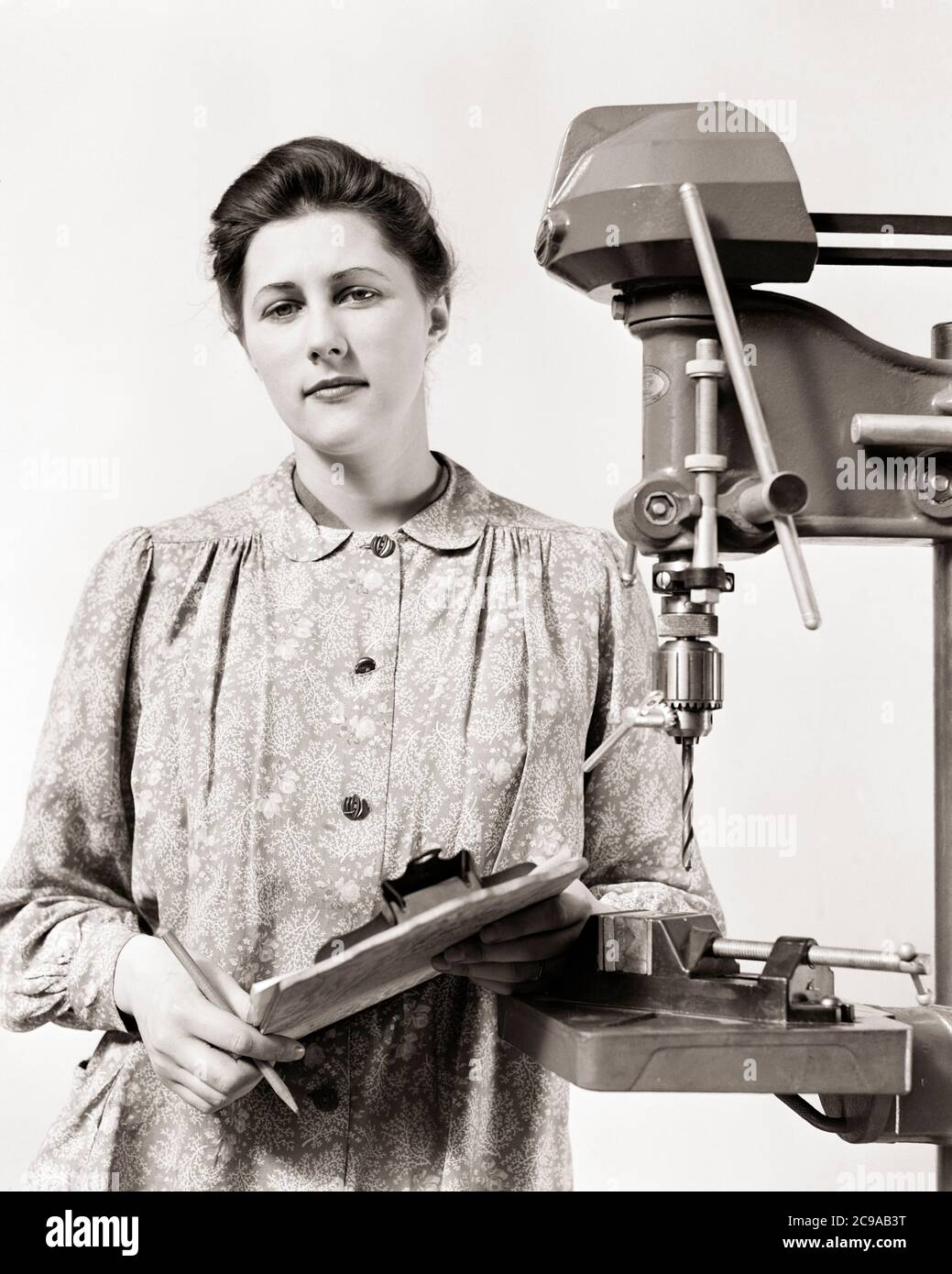 1940s SERIOUS WOMAN WW2 DEFENSE PRODUCTION SUPERVISOR STANDING BY DRILL PRESS WEARING SMOCK HOLDING CLIPBOARD LOOKING AT CAMERA - i3809 HAR001 HARS INSPIRATION SPIRITUALITY CONFIDENCE EXECUTIVES EXPRESSIONS B&W EYE CONTACT FREEDOM GOALS SUCCESS WELLNESS STRENGTH VICTORY STRATEGY COURAGE KNOWLEDGE LEADERSHIP POWERFUL PROGRESS WORLD WARS PRIDE WORLD WAR WORLD WAR TWO WORLD WAR II BY OPPORTUNITY SUPERVISOR AUTHORITY OCCUPATIONS BOSSES CONCEPTUAL SMOCK STYLISH SUPPORT WORLD WAR 2 SINCERE SOLEMN COOPERATION DEFENSE FOCUSED INTENSE MANAGERS PRECISION YOUNG ADULT WOMAN BLACK AND WHITE CAREFUL Stock Photo