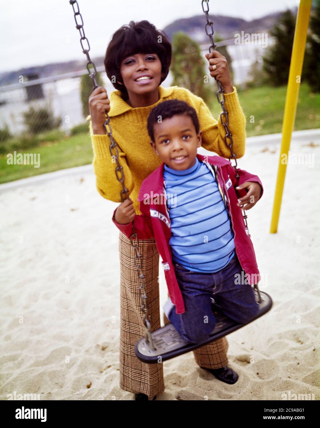 1970s AFRICAN-AMERICAN WOMAN MOTHER STANDING BEHIND HER SON BOY KNEELING ON PLAYGROUND SWING LOOKING AT CAMERA BOTH SMILING - kj5363 PHT001 HARS PAIR SUBURBAN COLOR HER MOTHERS OLD TIME NOSTALGIA OLD FASHION 1 FITNESS JUVENILE STYLE HEALTHY YOUNG ADULT SAFETY STRONG SONS PLEASED JOY LIFESTYLE FEMALES HOME LIFE COPY SPACE HALF-LENGTH LADIES PERSONS CARING MALES EYE CONTACT KNEELING ACTIVITY PHYSICAL CHEERFUL BOTH PROTECTION STRENGTH AFRICAN-AMERICANS AFRICAN-AMERICAN RECREATION BLACK ETHNICITY ON SMILES CONNECTION FLEXIBILITY JOYFUL MUSCLES PERSONAL ATTACHMENT AFFECTION EMOTION JUVENILES MOMS Stock Photo