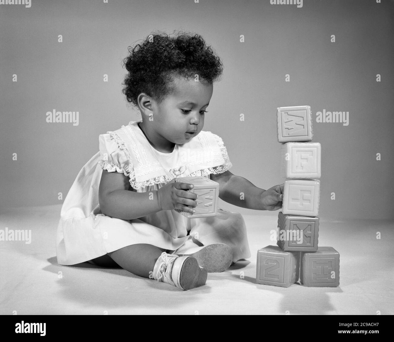 1960s BUSY CUTE AFRICAN-AMERICAN BABY GIRL TODDLER WEARING FRILLY DRESS OCCUPIED PLAYING WITH SET OF PLASTIC TOY BUILDING BLOCKS - n1989 HAR001 HARS 1 JUVENILE CUTE FACIAL STYLE BALANCE JOY LIFESTYLE FEMALES HEALTHINESS HOME LIFE COPY SPACE FULL-LENGTH CONFIDENCE EXPRESSIONS B&W GOALS SUCCESS HAPPINESS ADVENTURE DISCOVERY AFRICAN-AMERICANS AFRICAN-AMERICAN CHOICE EXCITEMENT KNOWLEDGE RECREATION BLACK ETHNICITY PRIDE FRILLY OF ENGROSSED CONCEPTUAL STYLISH OCCUPIED CREATIVITY GROWTH JUVENILES SOLUTIONS BLACK AND WHITE HAR001 OLD FASHIONED AFRICAN AMERICANS Stock Photo