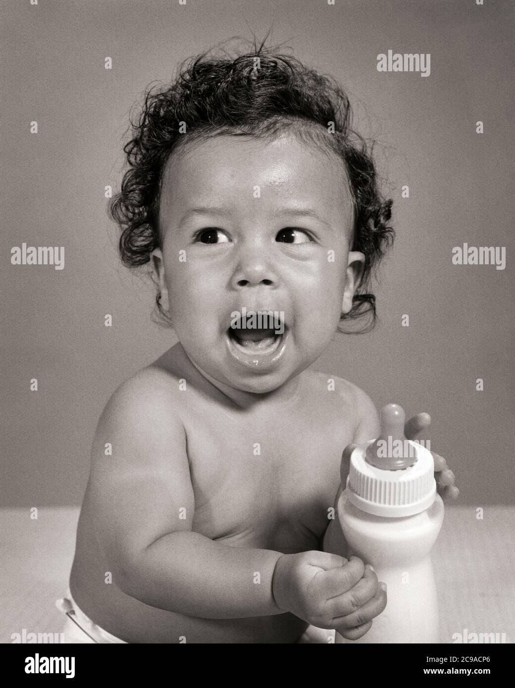 1960s SINGLE VOCALIZING AFRICAN-AMERICAN BABY BOY TODDLER SITTING HOLDING HIS OWN MILK BOTTLE  - n2149 HAR001 HARS PLEASED JOY LIFESTYLE HEALTHINESS HOME LIFE COPY SPACE HALF-LENGTH MALES B&W HUMOROUS HUNGRY WELLNESS CHEERFUL HIS AFRICAN-AMERICANS AFRICAN-AMERICAN EXCITEMENT LOUD BLACK ETHNICITY COMICAL SMILES CONCEPTUAL COMEDY JOYFUL STYLISH VOCALIZING COOPERATION GROWTH JUVENILES OWN BLACK AND WHITE HAR001 OLD FASHIONED AFRICAN AMERICANS Stock Photo