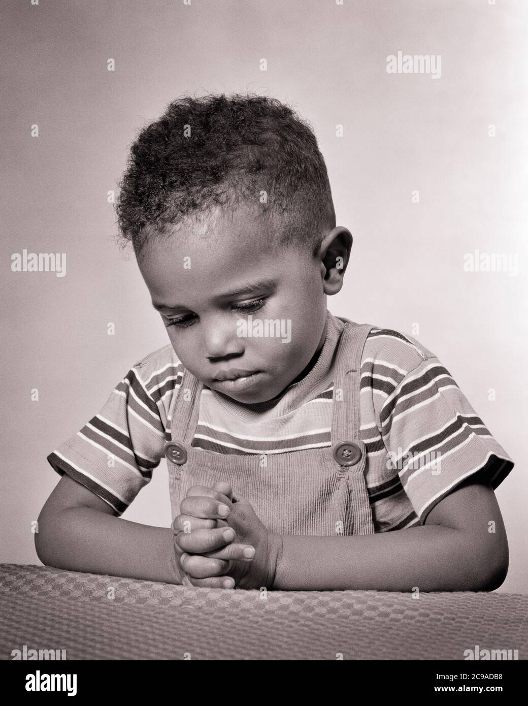1940s DEVOUT SERIOUS YOUNG AFRICAN-AMERICAN BOY WEARING T-SHIRT AND OVERALLS KNEELING SAYING HIS PRAYERS - n625 HAR001 HARS OVERALLS MALES SPIRITUALITY CONFIDENCE EXPRESSIONS B&W KNEELING TEMPTATION DREAMS HAPPINESS WELLNESS HIS STRENGTH AFRICAN-AMERICANS COURAGE AFRICAN-AMERICAN AND CHOICE BLACK ETHNICITY PRIDE CONCEPTUAL PRAYERS STYLISH SINCERE T-SHIRT SOLEMN FOCUSED GROWTH INTENSE JUVENILES BLACK AND WHITE CAREFUL DEVOUT EARNEST HAR001 INTENT OLD FASHIONED AFRICAN AMERICANS Stock Photo