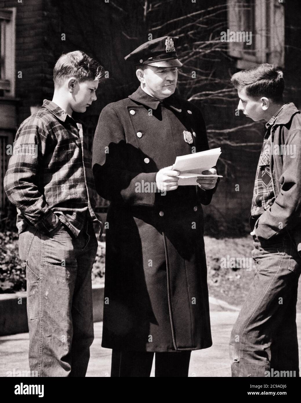 1940s 1950s TWO DEAD END TEENAGE BOYS ON THE STREET CONFRONTED BY POLICE OFFICER READING TRUANCY LETTER SUMMONS RULES WARRANT - w915 HAR001 HARS JUVENILE FEAR COMMUNICATION SERVE FRIEND LIFESTYLE COPY SPACE FRIENDSHIP HALF-LENGTH PERSONS CARING MALES ORDER OFFICER TEENAGE BOY B&W COP PROTECT AND SERVE PROTECT AND LEADERSHIP POWERFUL BY ON THE AUTHORITY OCCUPATIONS RULES UNIFORMS DELINQUENT FRIENDLY TEENAGED CONFRONTED OFFICERS POLICEMEN BEHAVIOR COOPERATION COPS ENFORCEMENT JUVENILES TRUANT BADGE BADGES BLACK AND WHITE CAUCASIAN ETHNICITY HAR001 OLD FASHIONED Stock Photo