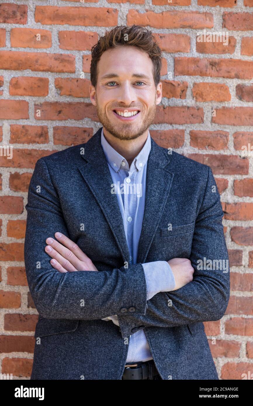 Happy smart casual businessman portrait on urban city brick wall background lifestyle portrait. Young professional man smiling confident in blazer Stock Photo