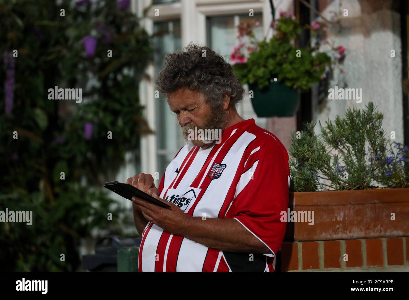 London, 29th July 2020  A supporter checks his phone as the game draws to a close outside Griffin Park on the final night of football at their historic home (Since 1904) before they move to their new ground, Brentford Community Stadium. They won their playoff semi-final to reach the final Andrew Fosker / Alamy Live News Stock Photo