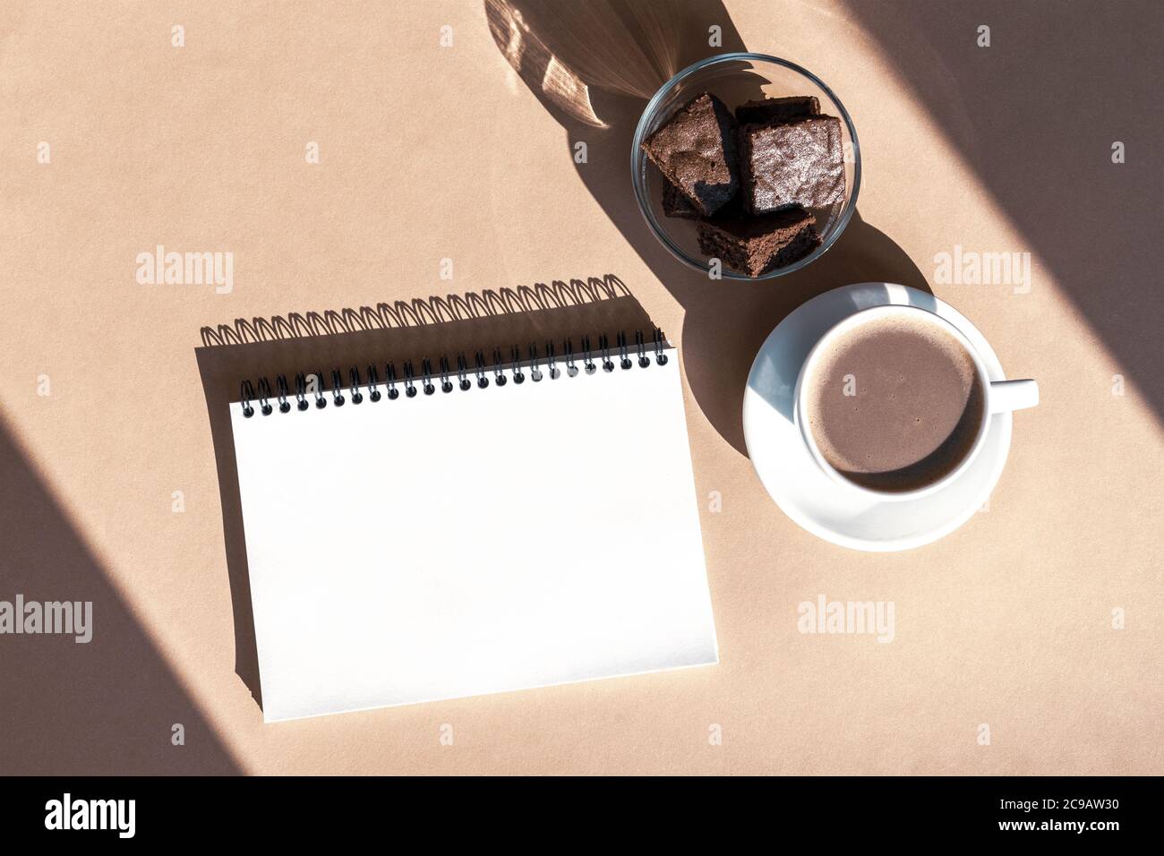 Notepad, coffee cup and chocolate cake. Cosy workplace, work at home concept. Sharp shadows, top view, flat lay, copy space Stock Photo