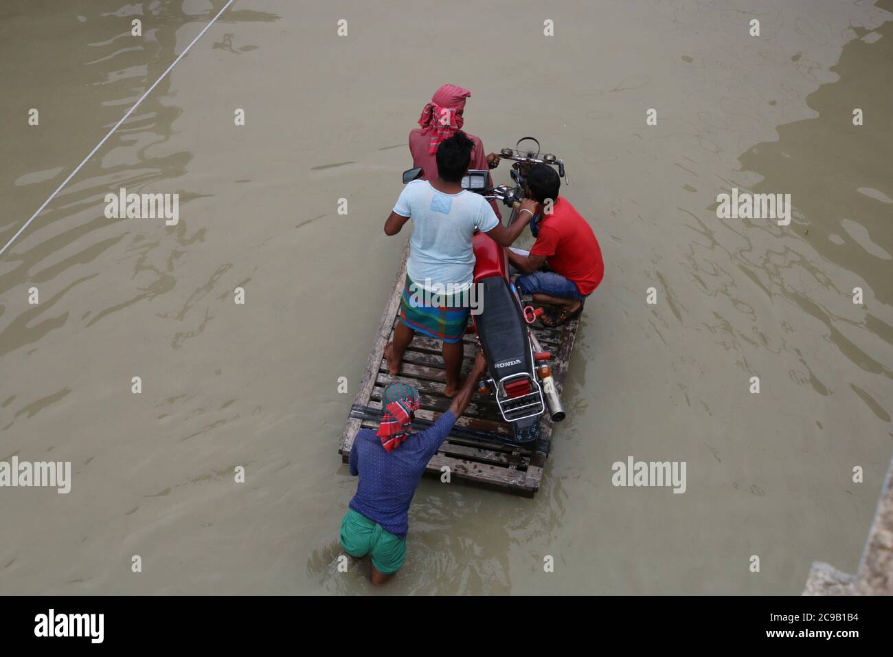 People seen transporting a motor bike on a three wheeler van as the road is submerged by flood water.One third of Bangladesh is under water after some of the heaviest rains in a decade leaving more than 3 million people affected with homes and roads in villages flooded, Flood Forecasting and Warning Centre (FFWC) officials said. Stock Photo