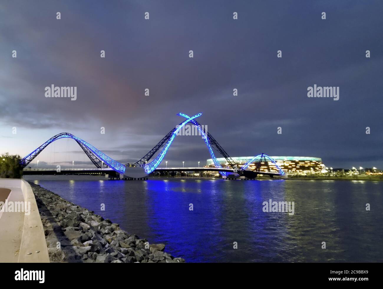 Night view to the Perth Matagarup bridge and with blue neon lights and reflections on the Swan River. Optus Stadium with dark sky on a background. Stock Photo