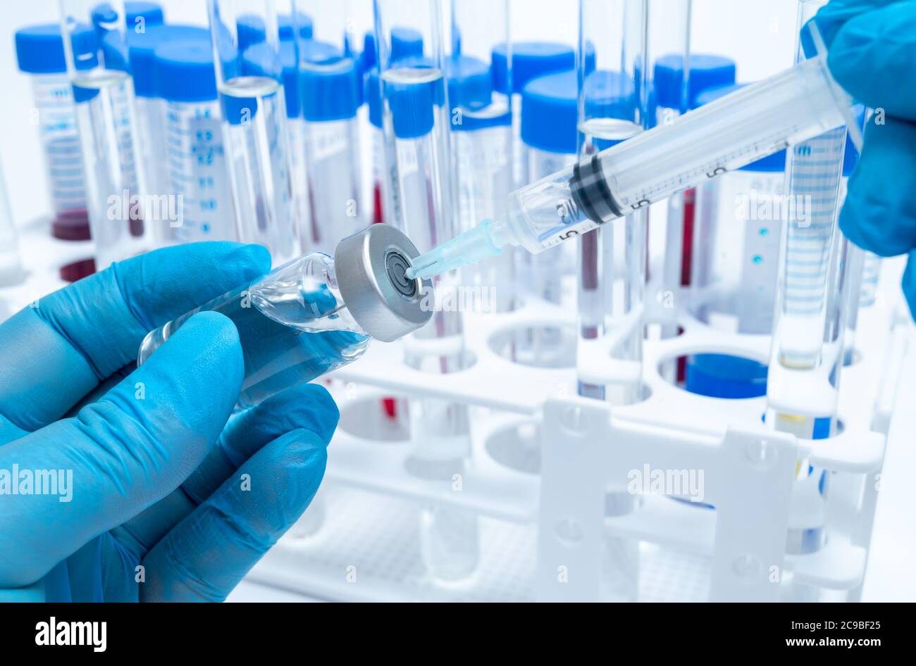 Scientist's hand wearing blue gloves and holding an ampoule and syringe. Stock Photo