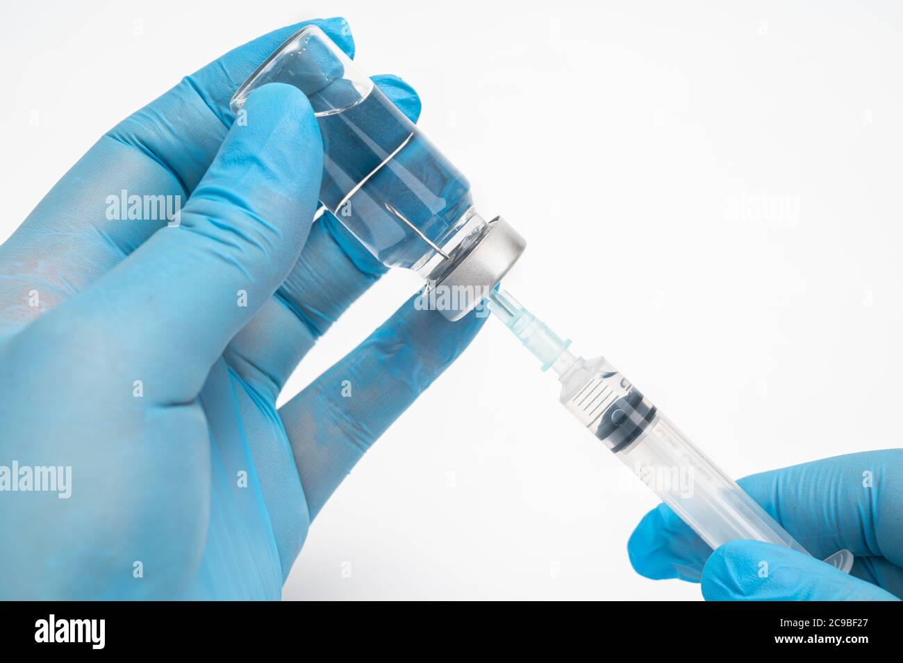 Scientist's hand wearing blue gloves and holding an ampoule and syringe. Stock Photo